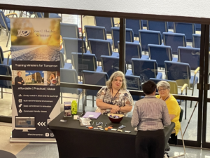 Picture of two Fletcher representatives at a Fletcher exhibit table, speaking with a conference attendee